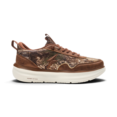 A single low-top sneaker shown in a side profile on a clean white background. The upper features a brown and brown camouflage pattern with solid brown leather overlays, a brown side logo, and a thick off-white sole.